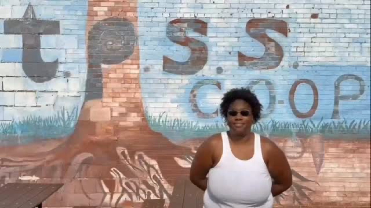 A community member stands in front of the TPSS Co-op mural.